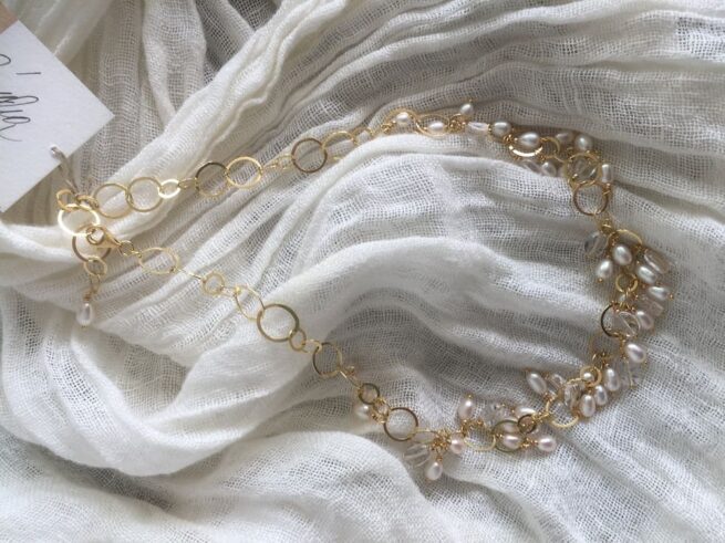 collana girocollo argento dorato perle nome Mizar distesa su sciarpa bianca stropicciata