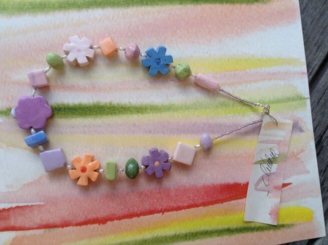 collana girocollo ceramica lavorata amano fiori multicolori di nome Primavera distesa su quadro