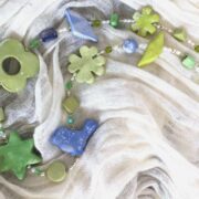 collana verde azzurra ceramica a mano di nome Menta distesa su sciarpa bianca plissettata