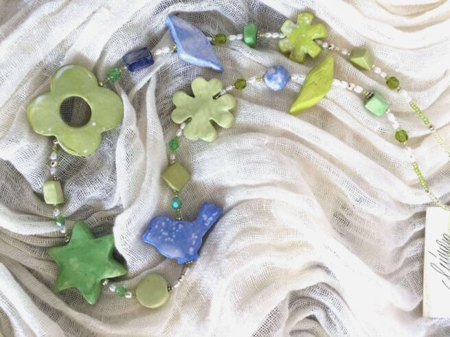 collana verde azzurra ceramica a mano di nome Menta distesa su sciarpa bianca plissettata