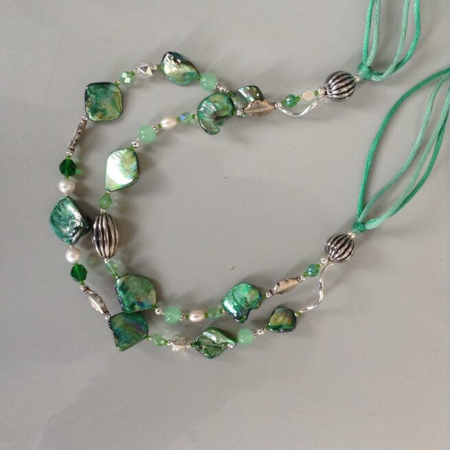collana verde madreperla due fili di nome Luminosa Verde giada perle cristalli distesa sfondo grigio chiaro