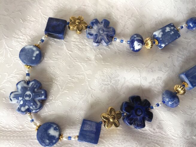 collana girocollo ceramica lavorata a mano blu fiori di nome Zaffiro distesa su stoffa bianca