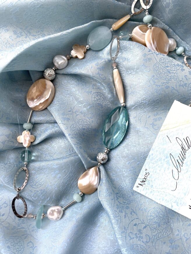 collana beige-verde acqua madreperla ossidiana chiamata Naxos distesa su sciarpa azzurra