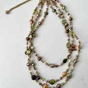 collana marrone verde perle fiume tre giri di nome Bagliori distesa sfondo bianco